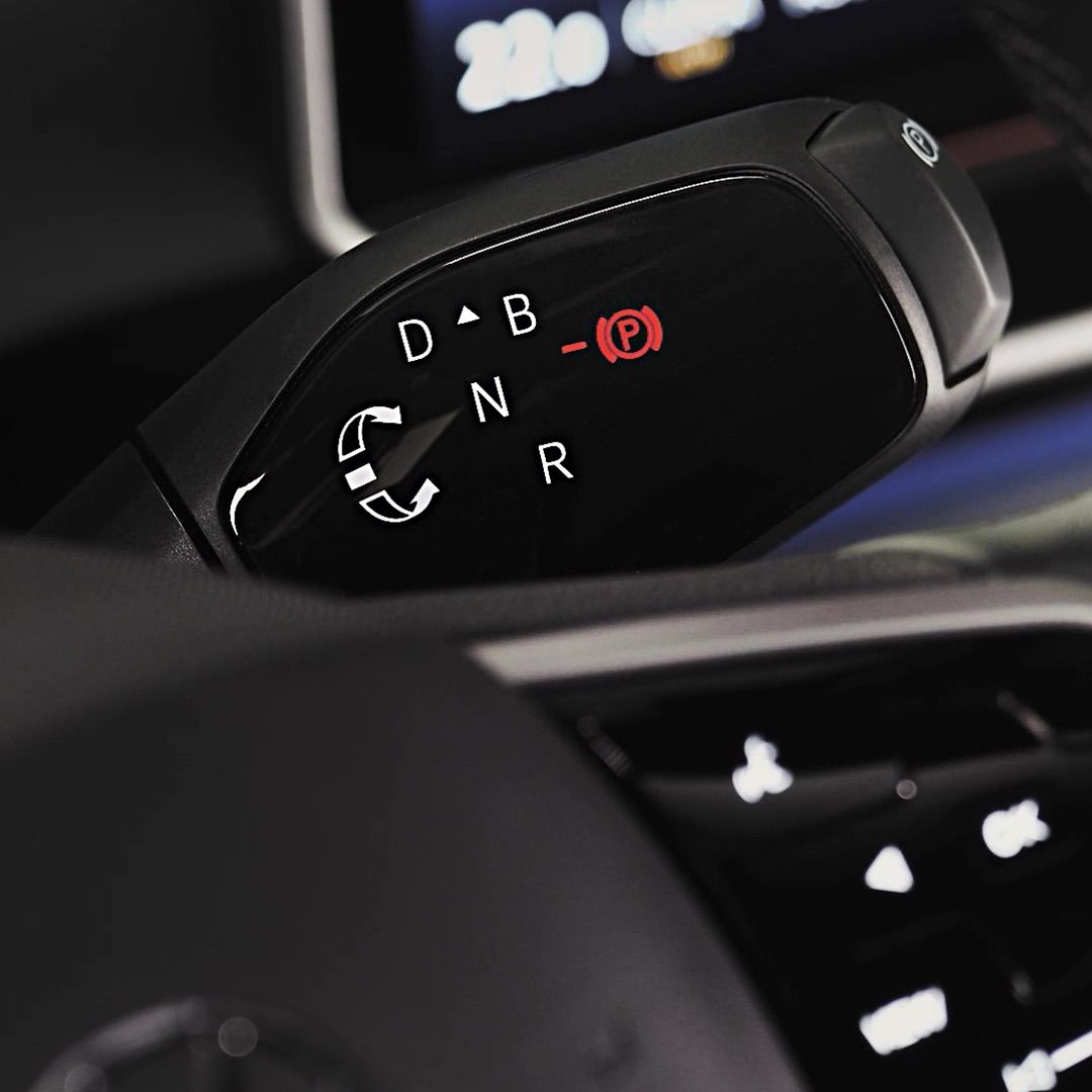 Nahaufnahme eines Automatikgetriebeschalters in einem Auto. Die Positionen D, B, N und R sind auf dem Schalthebel sichtbar. Im Hintergrund ist ein Teil des Armaturenbretts erkennbar.