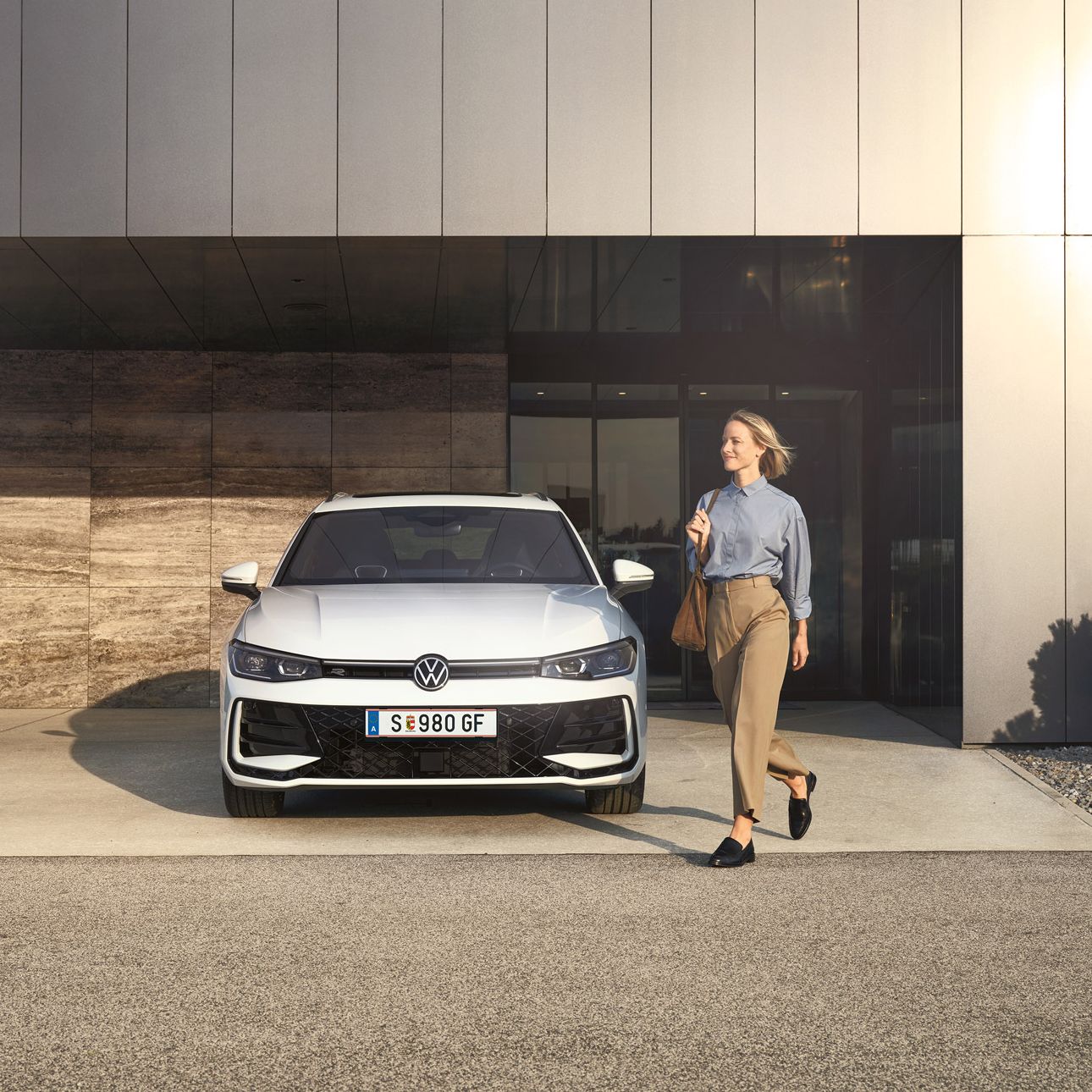 Frontansicht eines weißen VW Passat R-Line, eine Frau geht an ihm vorbei.