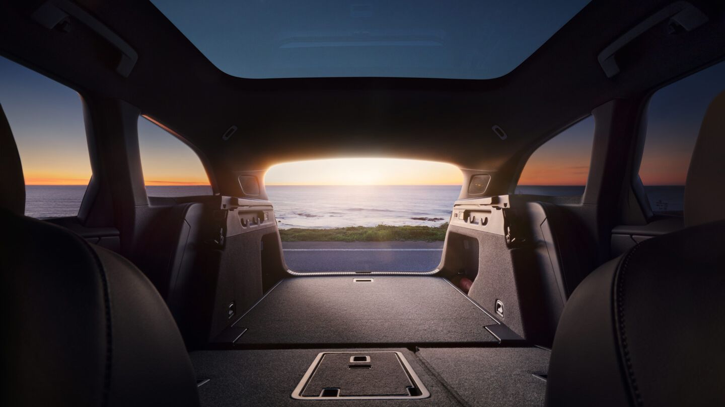 Blick aus dem geöffneten Kofferraum mit umgeklappter Rücksitzbank aus dem ID.7 Tourer auf einen Sonnenuntergang über dem Meer. 