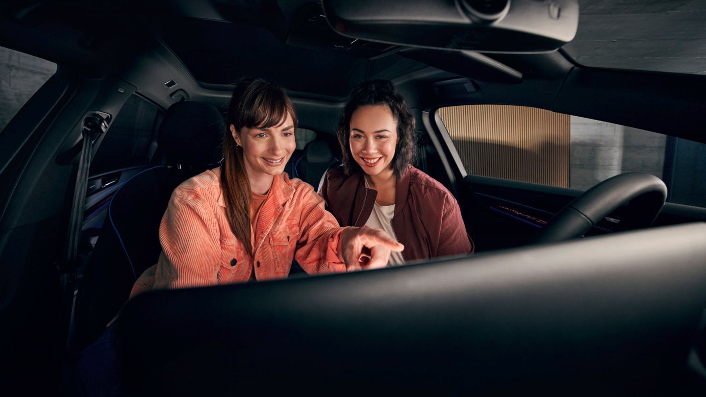 Zwei junge Frauen sitzen vorn im VW ID.7 und schauen auf das Infotainment-System.