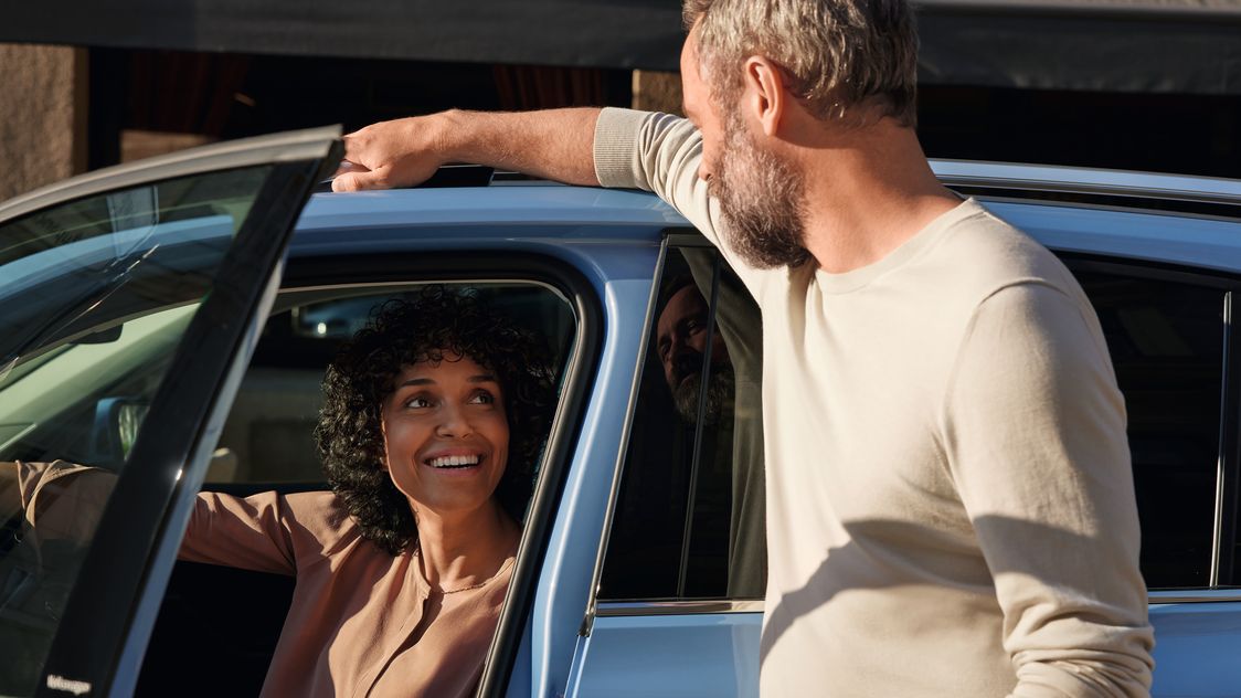 Mann redet mit einer Frau, die am Fahrersitz eines blauen VW T-Cross sitzt