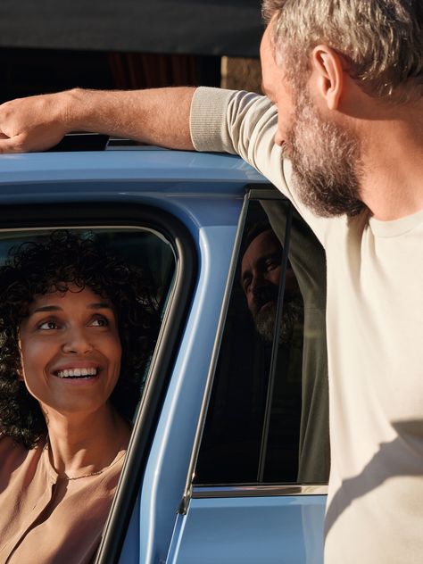 Mann redet mit einer Frau, die am Fahrersitz eines blauen VW T-Cross sitzt