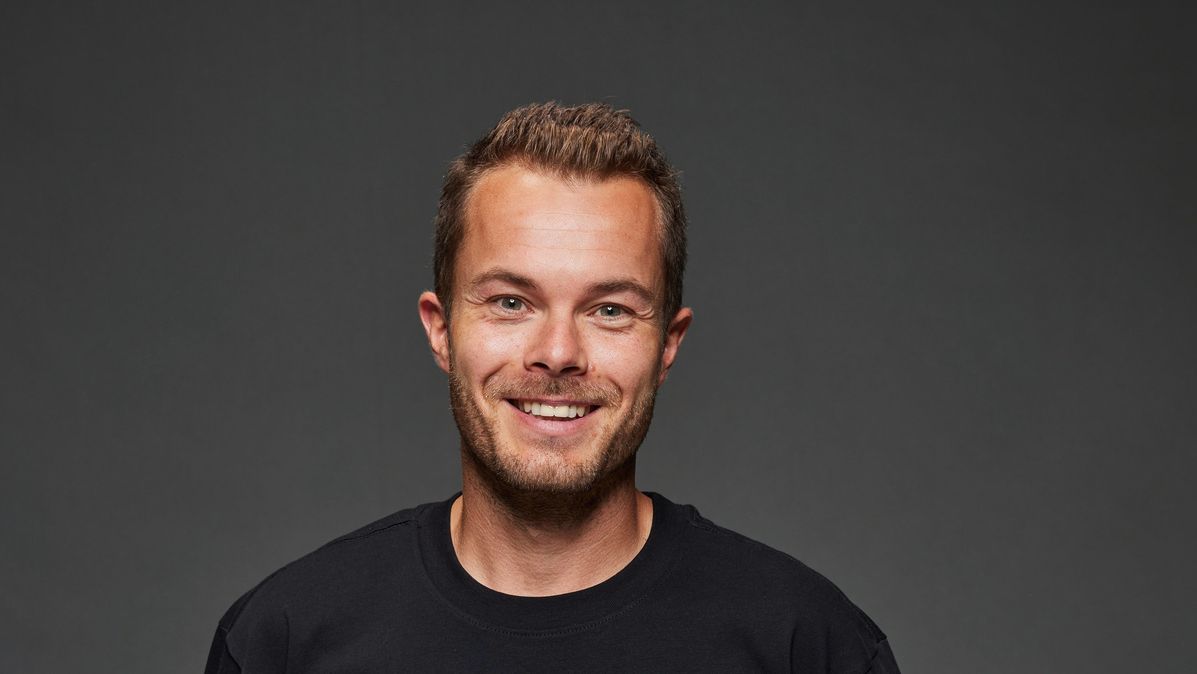 Motorsportprofi und Markenbotschafter Benjamin Leuchter. Das Bild zeigt ihn in einem schwarzen Shirt und grauer Jeans vor dunklem Hintergrund, in die Kamera lächelnd.