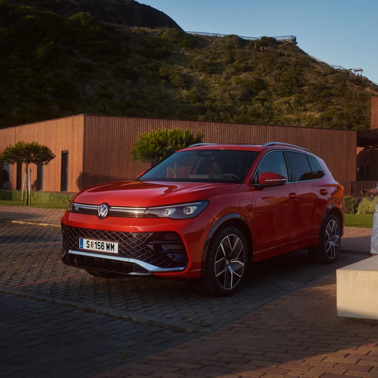 Frontansicht eines roten VW Tiguan auf einem Parkplatz. Eine Frau und ein Junge mit einem Skateboard gehen auf den Wagen zu.