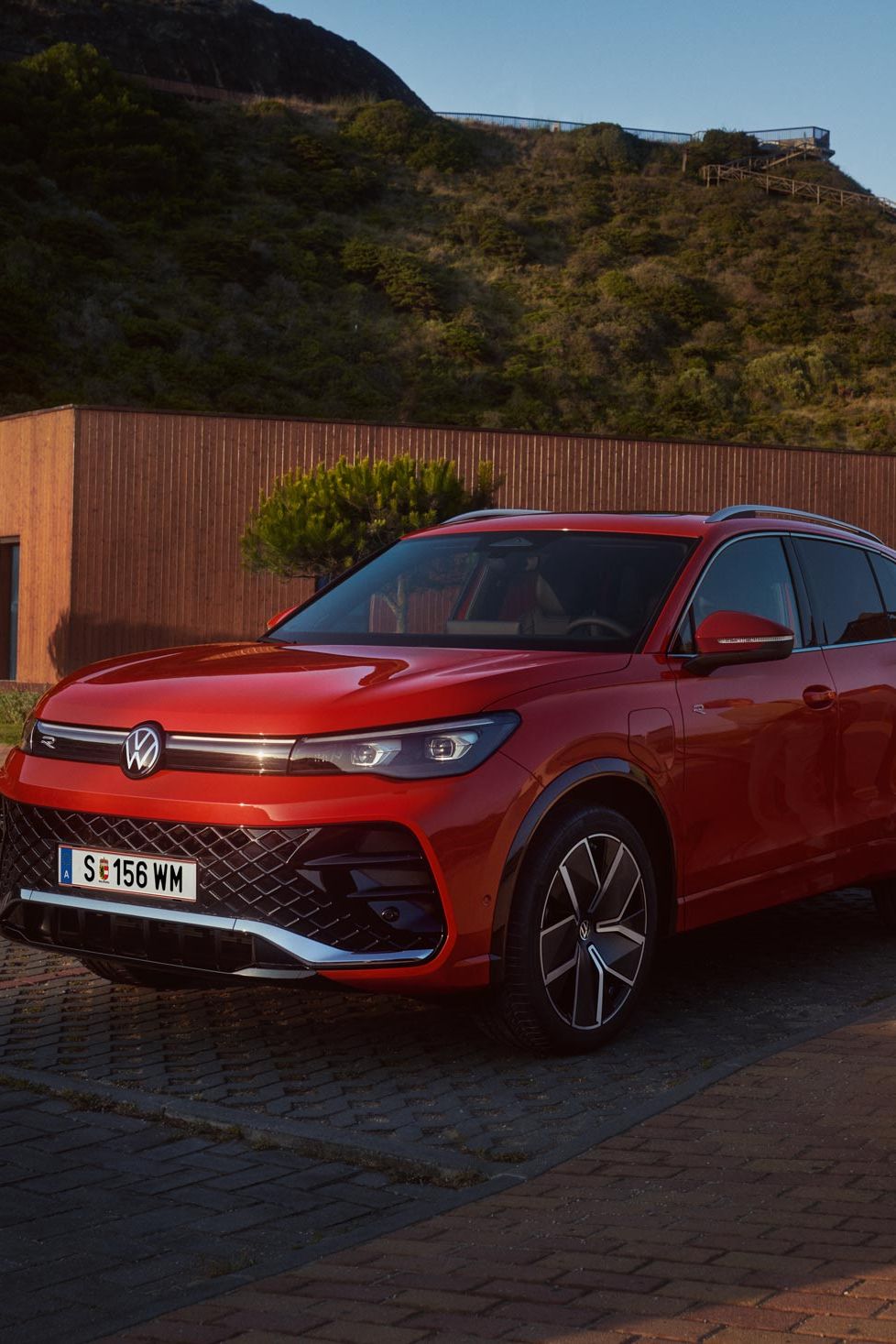 Frontansicht eines roten VW Tiguan auf einem Parkplatz. Eine Frau und ein Junge mit einem Skateboard gehen auf den Wagen zu.