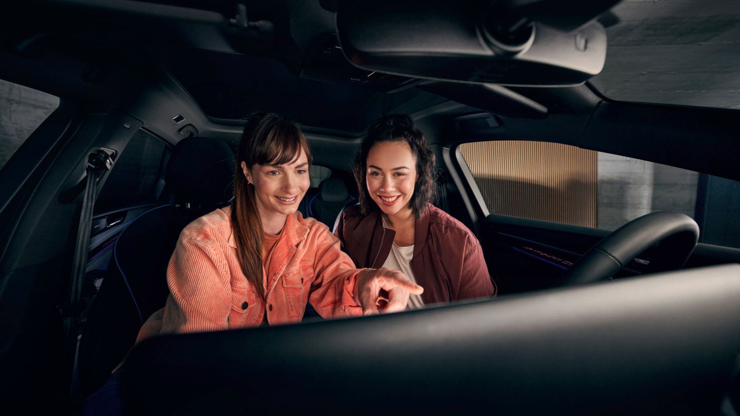 Zwei junge Frauen sitzen vorn im VW ID.7 und schauen auf das Infotainment-System.