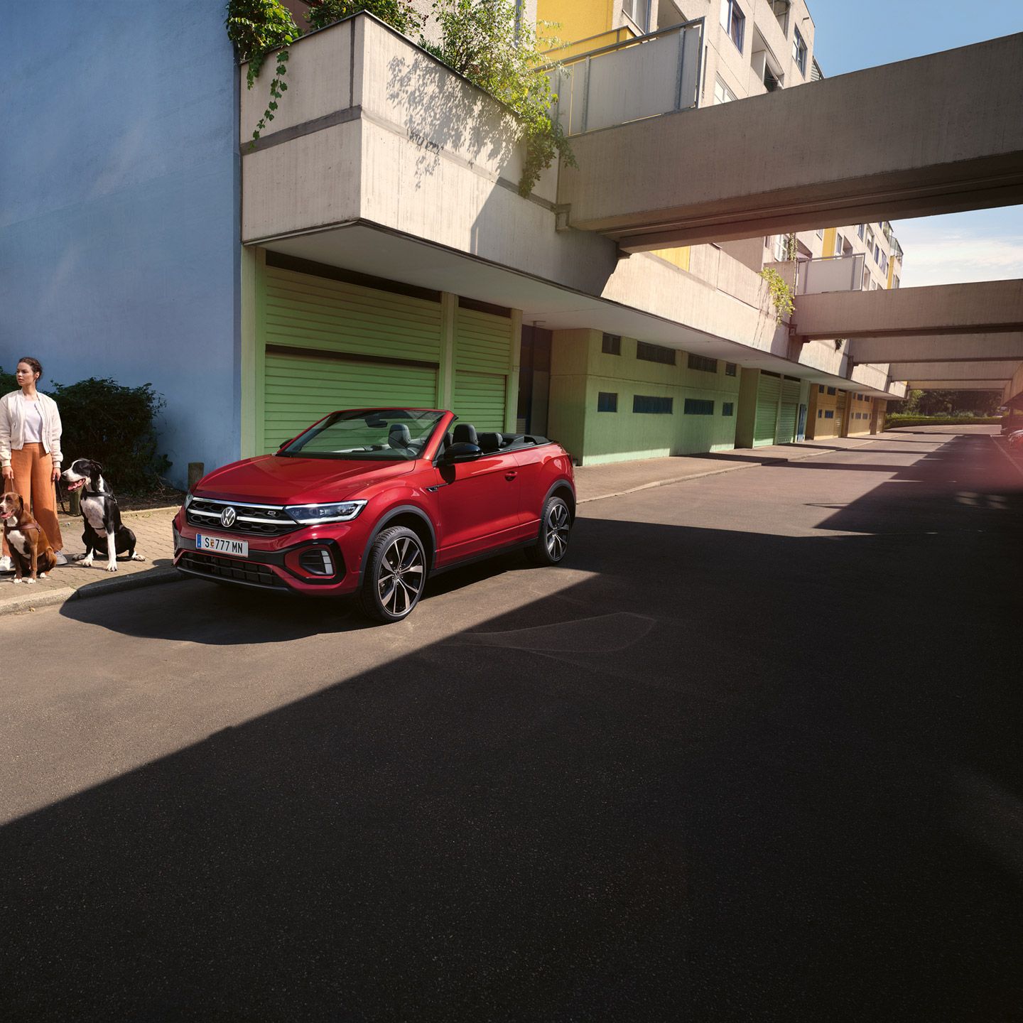 Eine Frau steht mit zwei Hunden neben einem roten VW T-Roc Cabrio