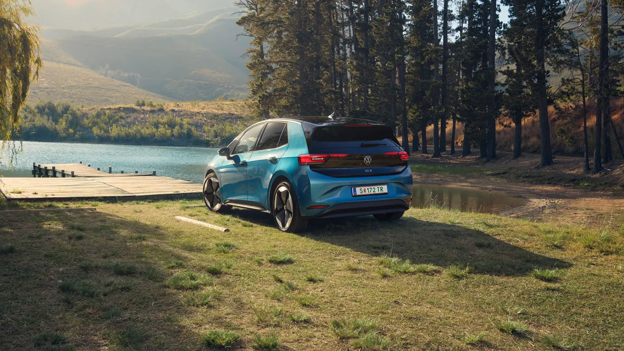 Ein blauer ID.3 steht am Ufer eines Sees, umgeben von hohen Bäumen.