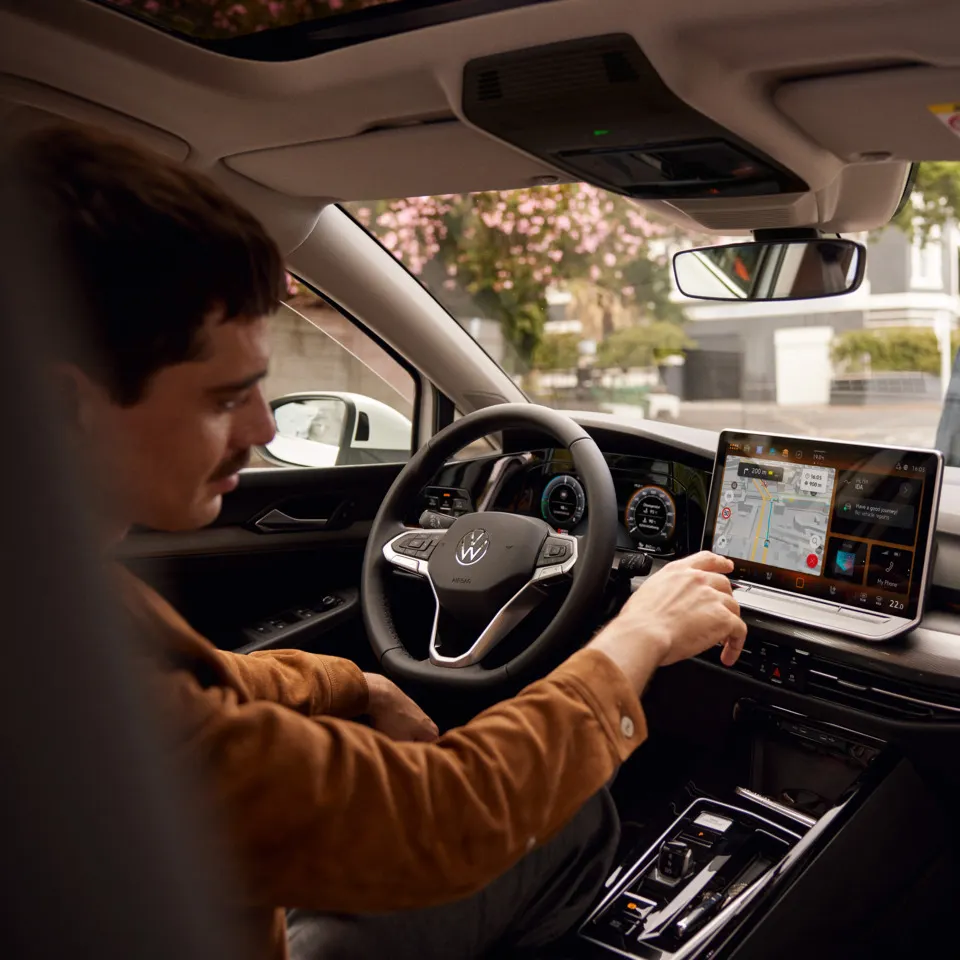 Ein Mann sitzt im parkenden VW Golf und bedient das Navigationssystem.