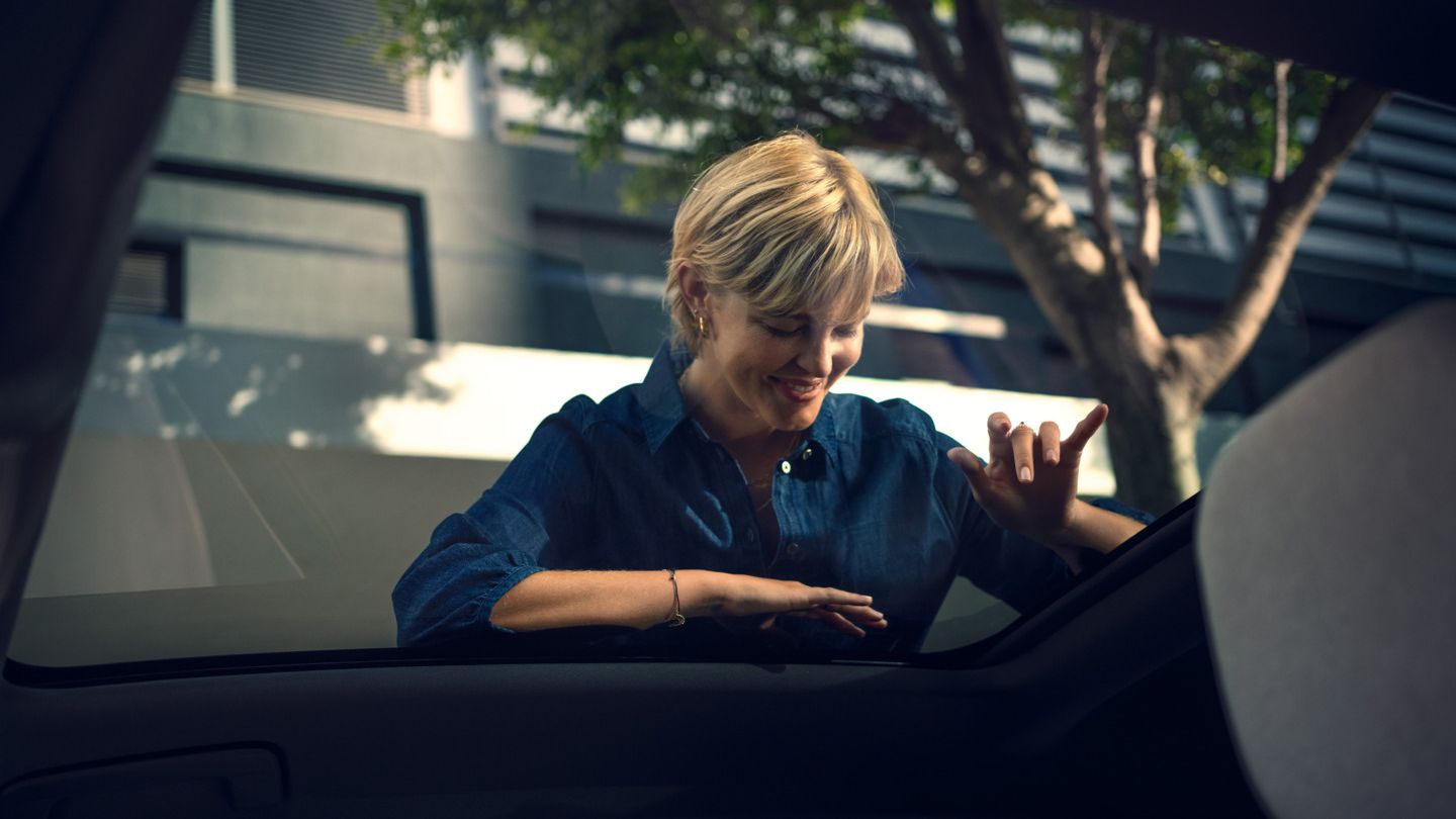 Eine Frau schaut von außen durch das Panoramadach in einen VW ID. Polo Style hinein und winkt jemanden zu.
