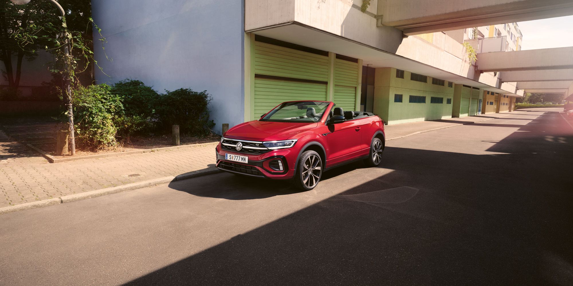 Roter T-Roc Cabriolet steht geparkt am Straßenrand neben dem Gehsteig in einer Stadt.