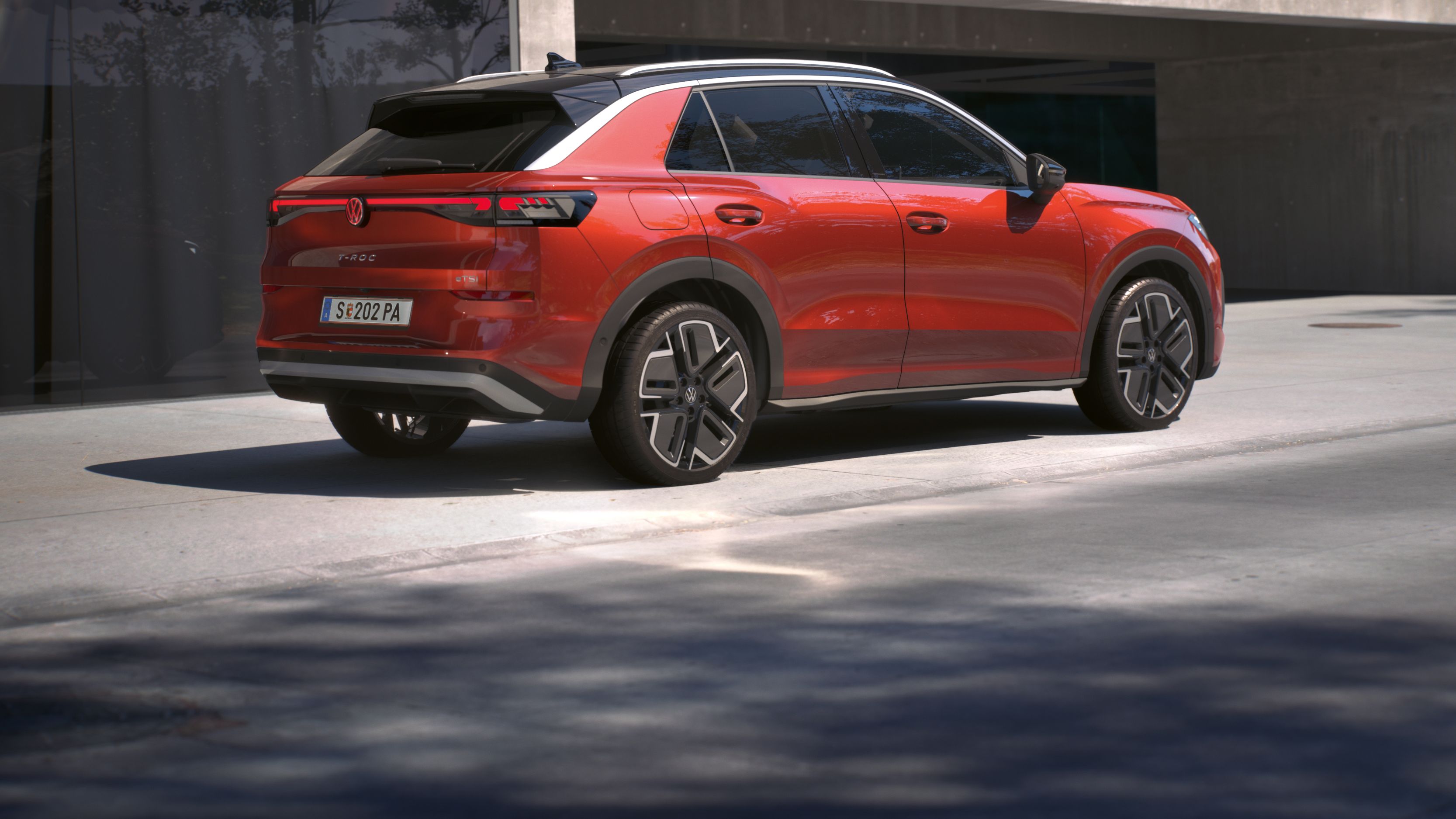 Eine 3/4-Rückansicht eines roten Volkswagen T-Roc Style, parkend vor einem Gebäude.