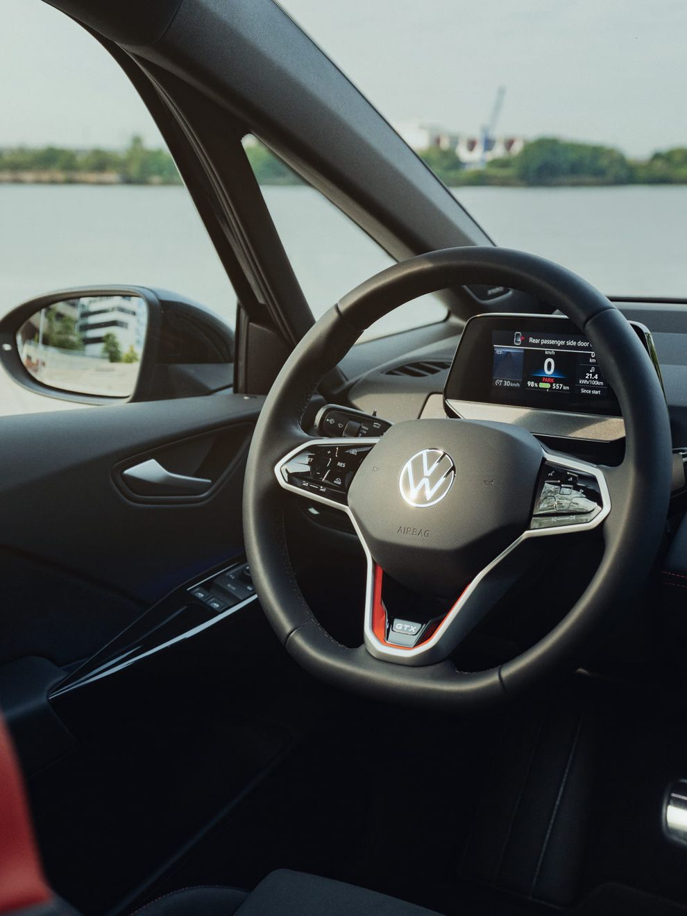 Das Bild zeigt das Lenkrad und das Armaturenbrett des ID.3 GTX FIRE+ICE, welcher am Wasser geparkt ist. Das Navigationsgerät auf dem Armaturenbrett zeigt eine Karte an. Die Sitze sind schwarz mit roten Akzenten.