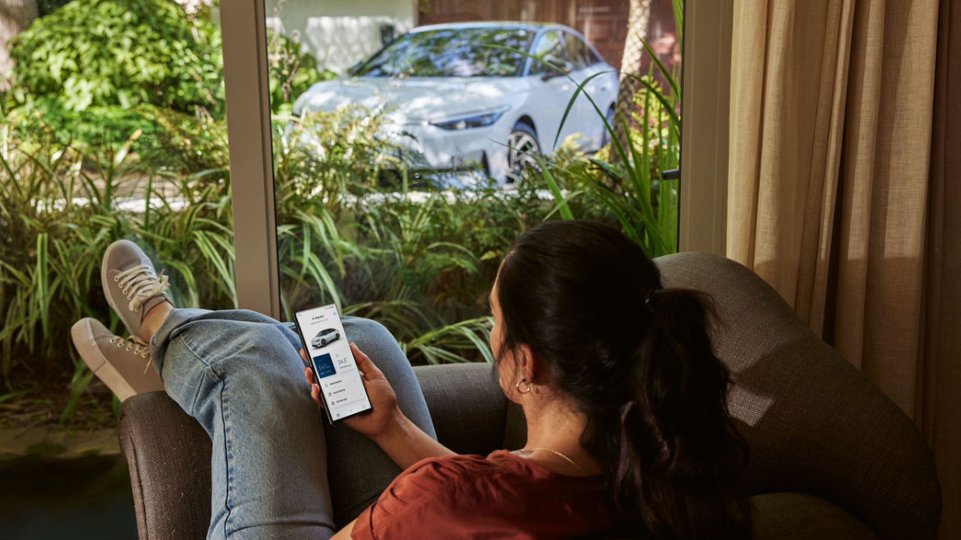 Person liegt auf Couch mit Smartphone in der Handy und schaut sich ein Auto an.
