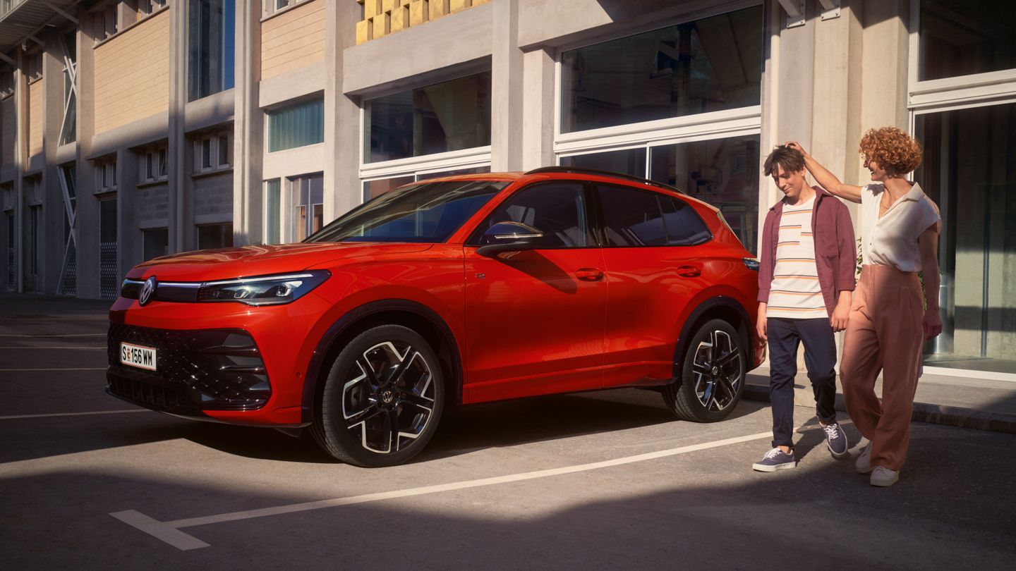 Mutter legt ihre Hand den Kopf ihres Sohnes, beiden gehen neben eines roten VW Tiguan R-Line her