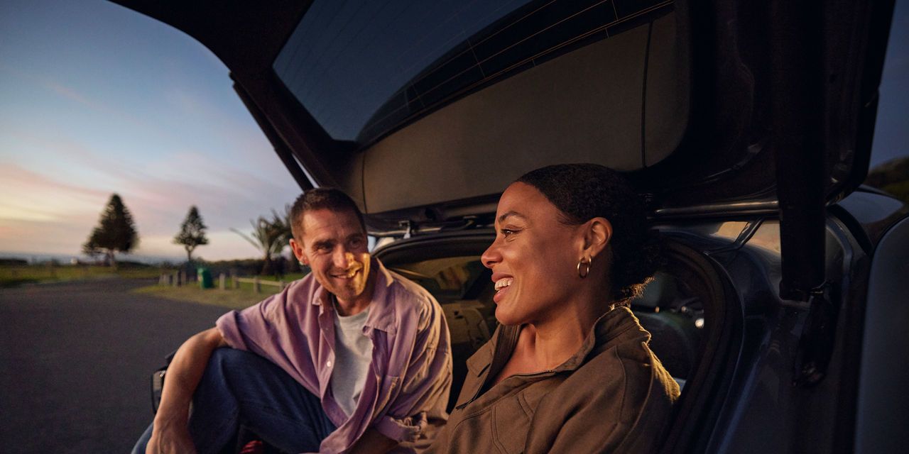 Ein Mann und eine Frau sitzen unter der geöffneten Heckklappe eines Volkswagen ID.7 Tourers