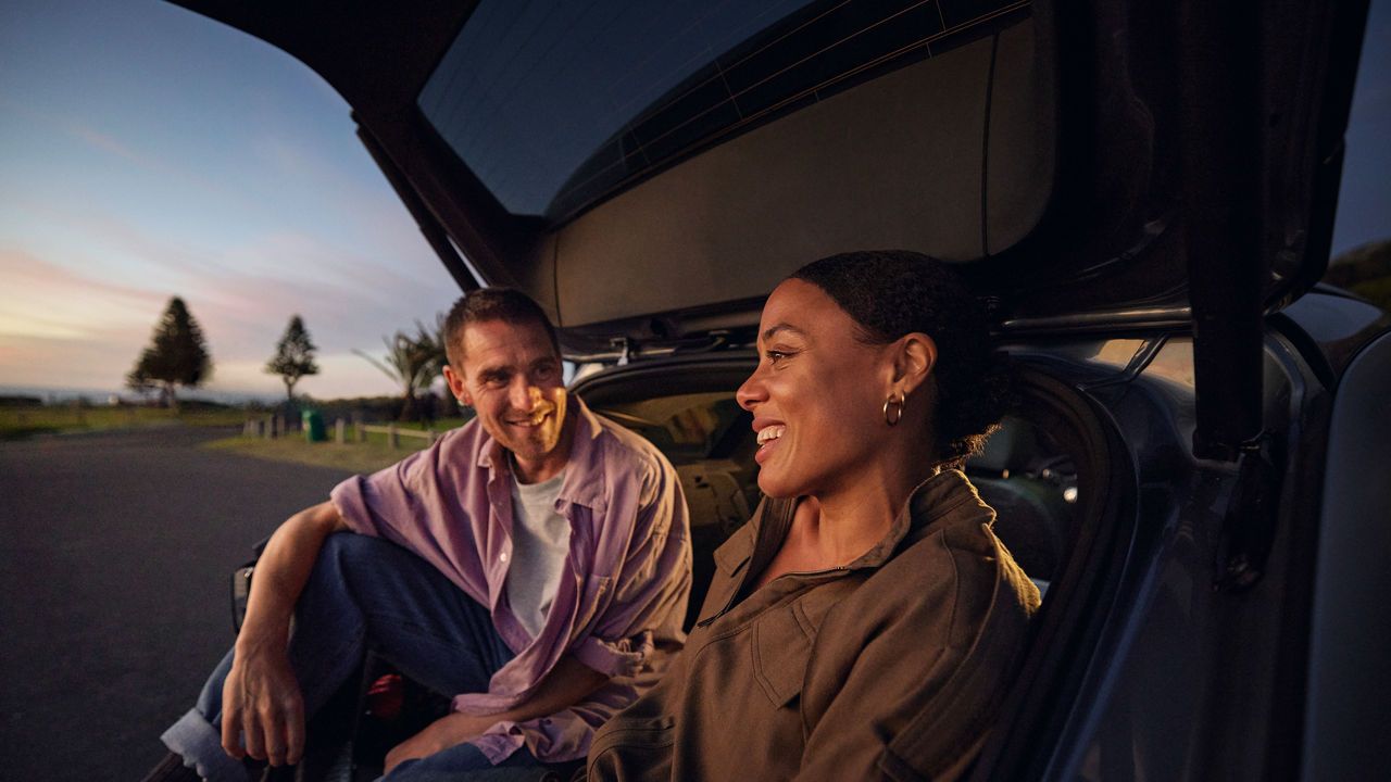 Ein Mann und eine Frau sitzen unter der geöffneten Heckklappe eines Volkswagen ID.7 Tourers