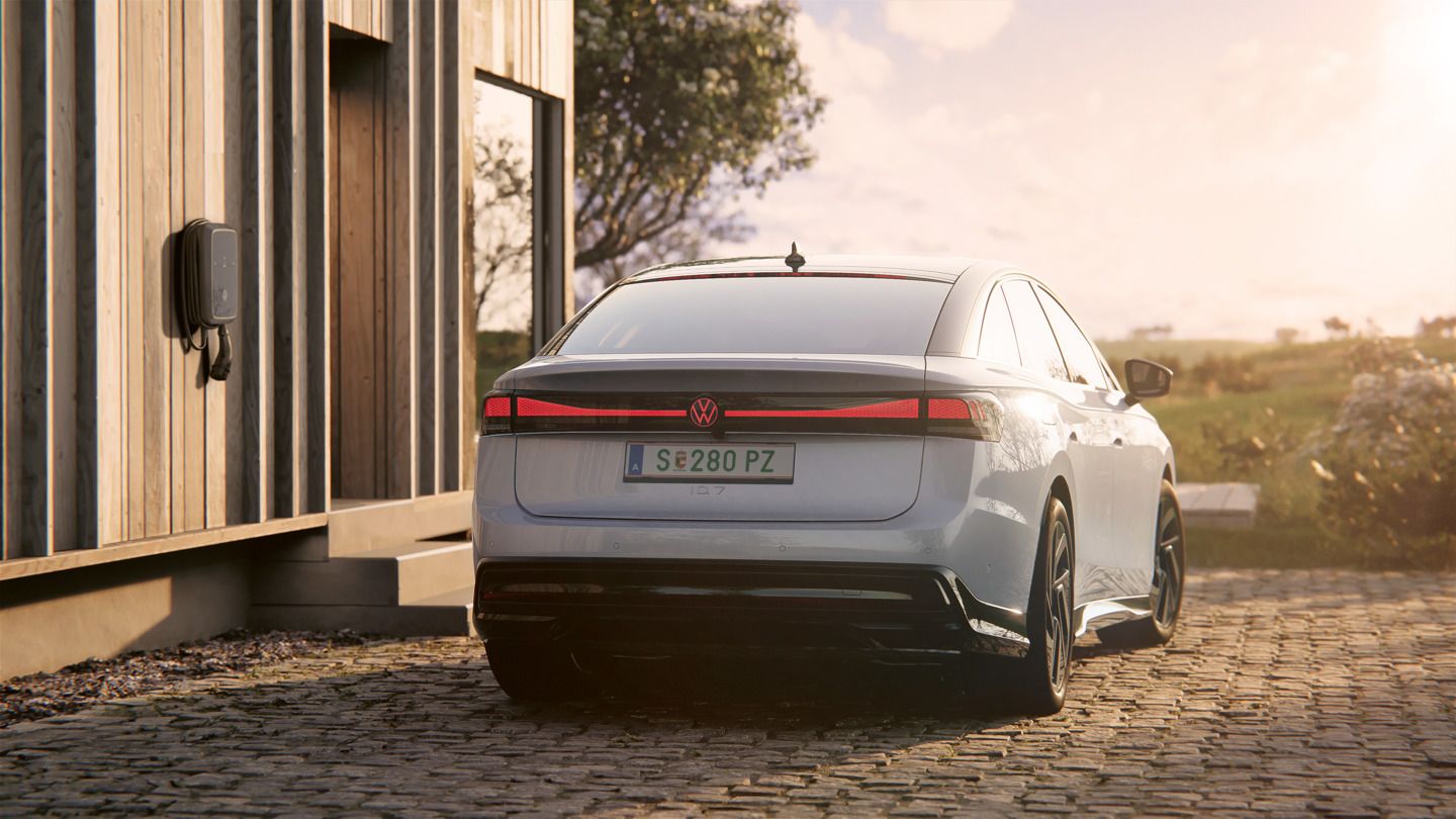 Heckansicht eines weißen VW ID.7, der neben einer Ladesäule steht. Die Heck-Lichtsignatur mit Volkswagen-Logo leuchtet rot.