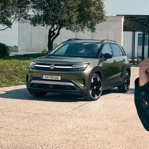 Ein Mann macht ein Selfie mit einem grünen VW ID. Cross, der auf der Auffahrt eines Gebäudes parkt.