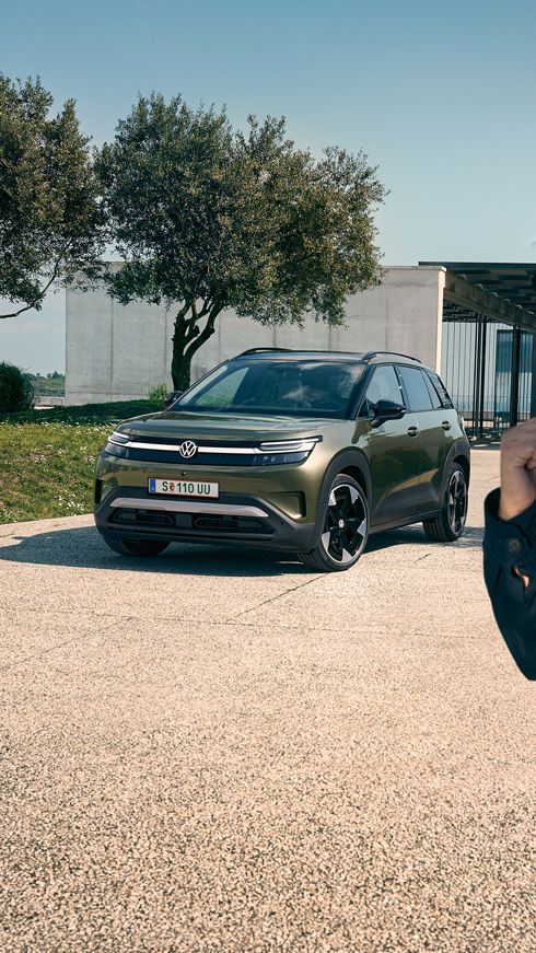 Ein Mann macht ein Selfie mit einem grünen VW ID. Cross, der auf der Auffahrt eines Gebäudes parkt.