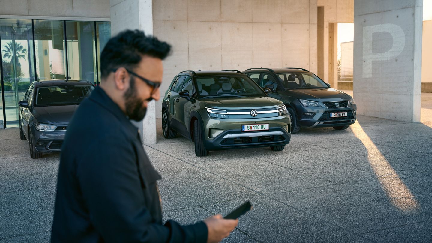 Ein Mann schaut auf sein Smartphone, im Hintergrund fährt ein VW ID. Cross automatisch in eine Parklücke.