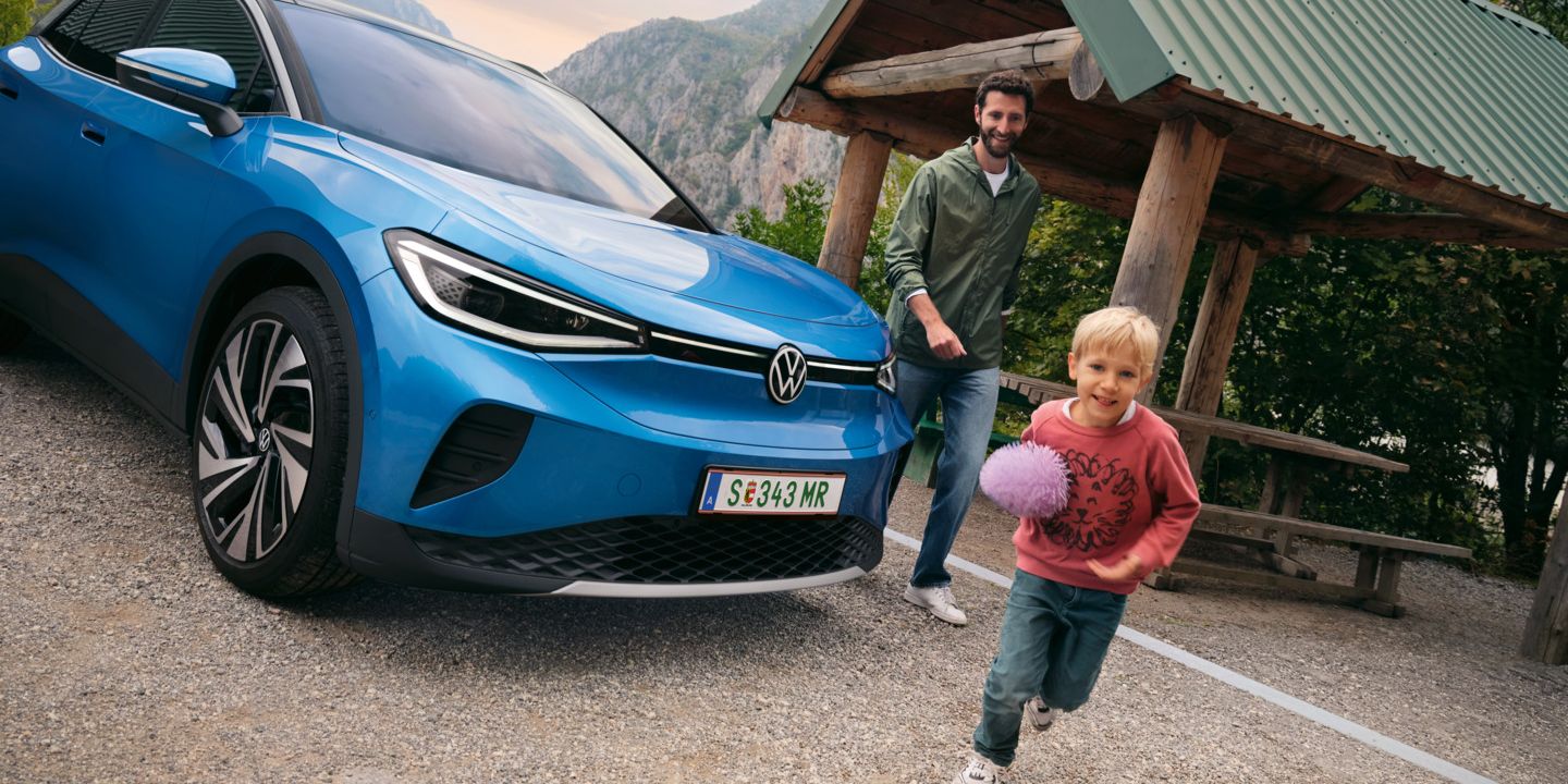 Vater und Sohn spielen mit einem Ball, daneben steht ein blauer VW ID.4.