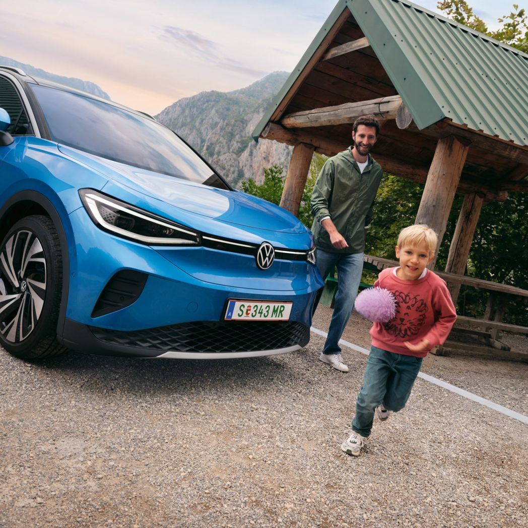 Vater und Sohn spielen mit einem Ball, daneben steht ein blauer VW ID.4.