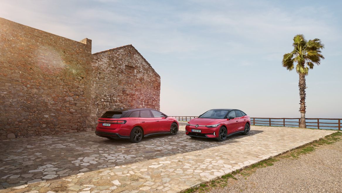 Ein roter ID.7 GTX und ID.7 Tourer GTX stehen nebeneinander vor einem Steinhaus mit Bick auf das Meer. 
