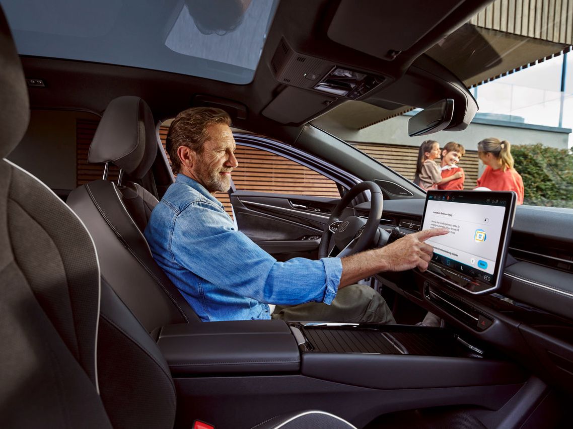 Mann sitzt in seinem Volkswagen und berührt das Display, im Hintergrund seine Familie