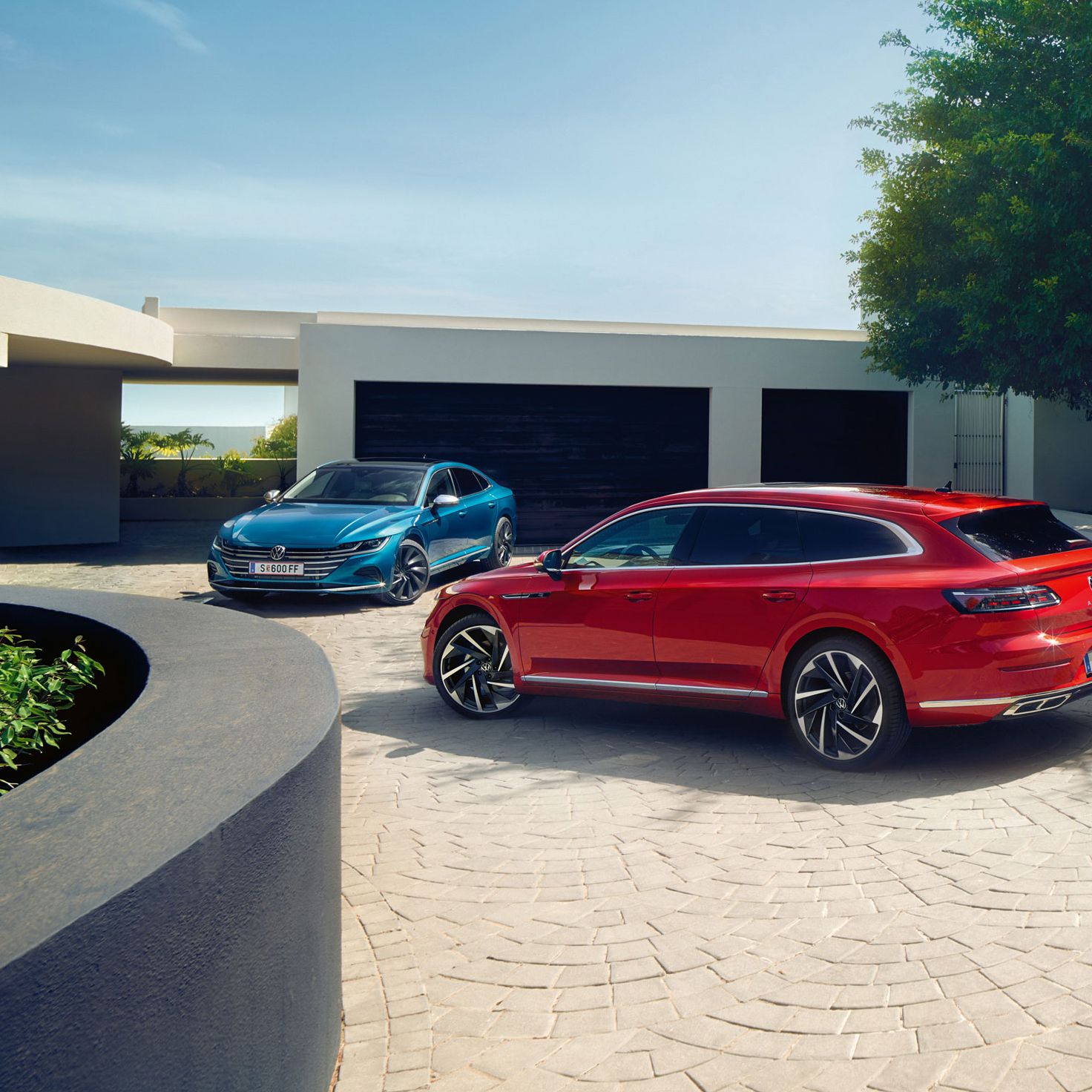 Zwei Arteon sind vor einem eleganten Haus mit weißer Fassade und schwarzen Garagentoren geparkt. Ein rotes Auto steht im Vordergrund, während ein blaues Auto im Hintergrund nahe der Garage parkt. Die Szene ist von klarem Himmel und grünen Pflanzen umgeben.