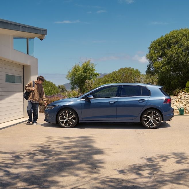 Ein junger Mann geht an einem blauen VW Golf vorbei