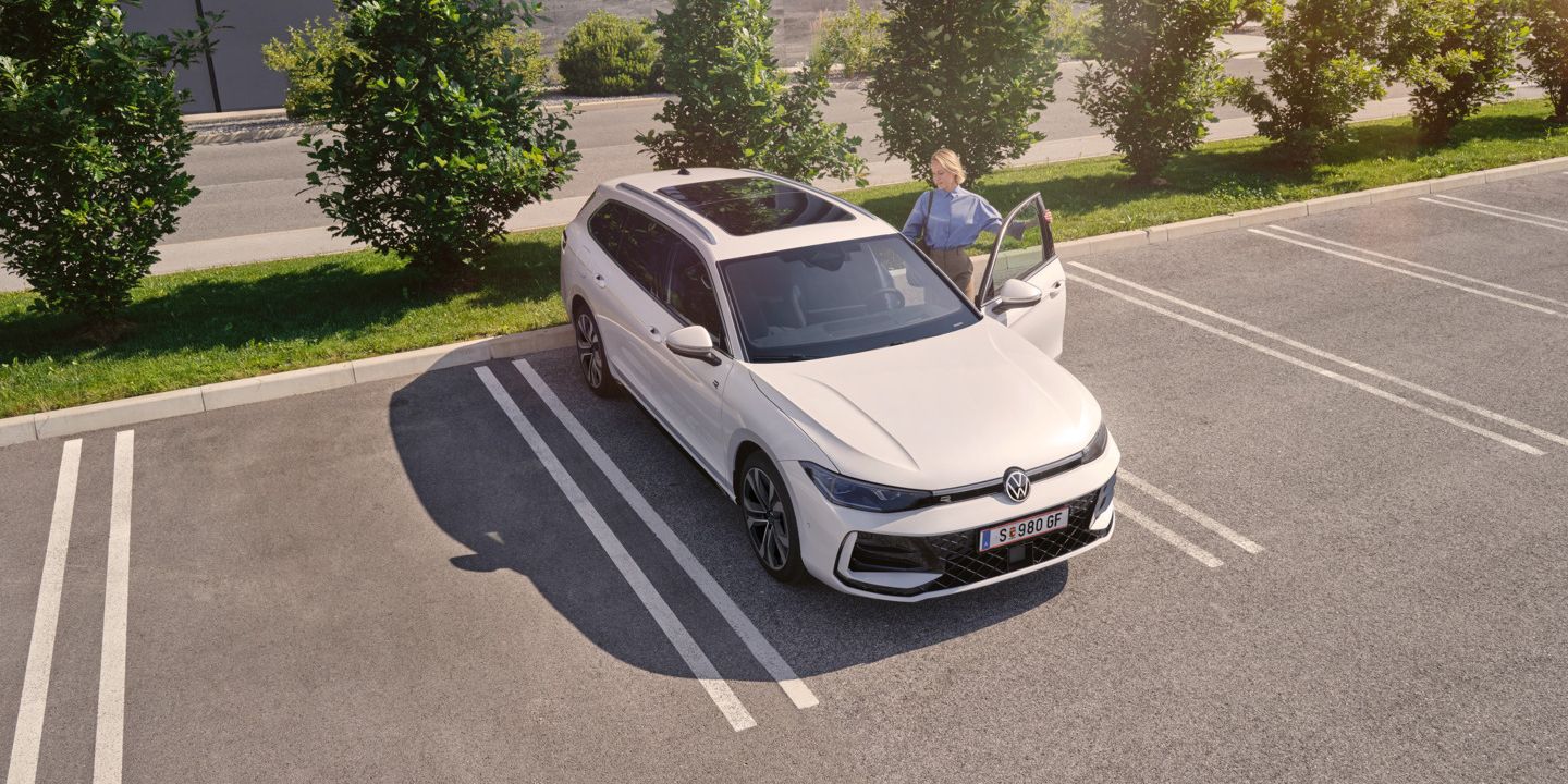 Weißer VW Passat parkt vor einem modernen Bürogebäude. Eine Frau steigt ein.