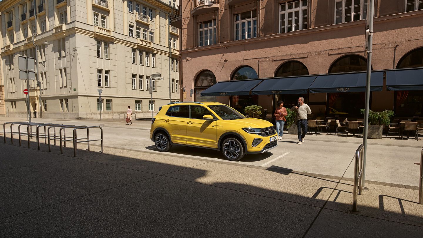 Ein geparkter T-Cross am Straßenrand, auf den 2 Personen von der anderen Straßenseite zugehen