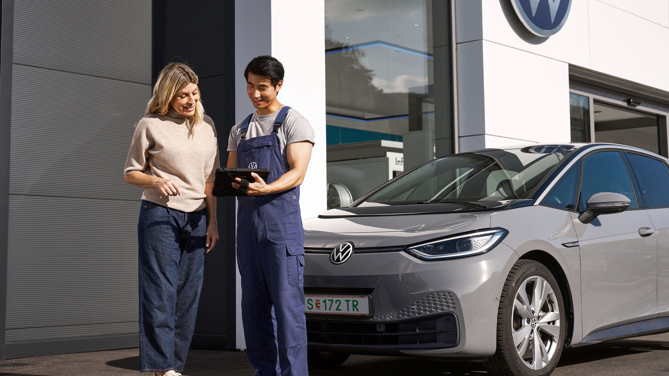 Ein Volkswagen Techniker und eine Kundin stehen vor einem grauen Volkswagen ID.3