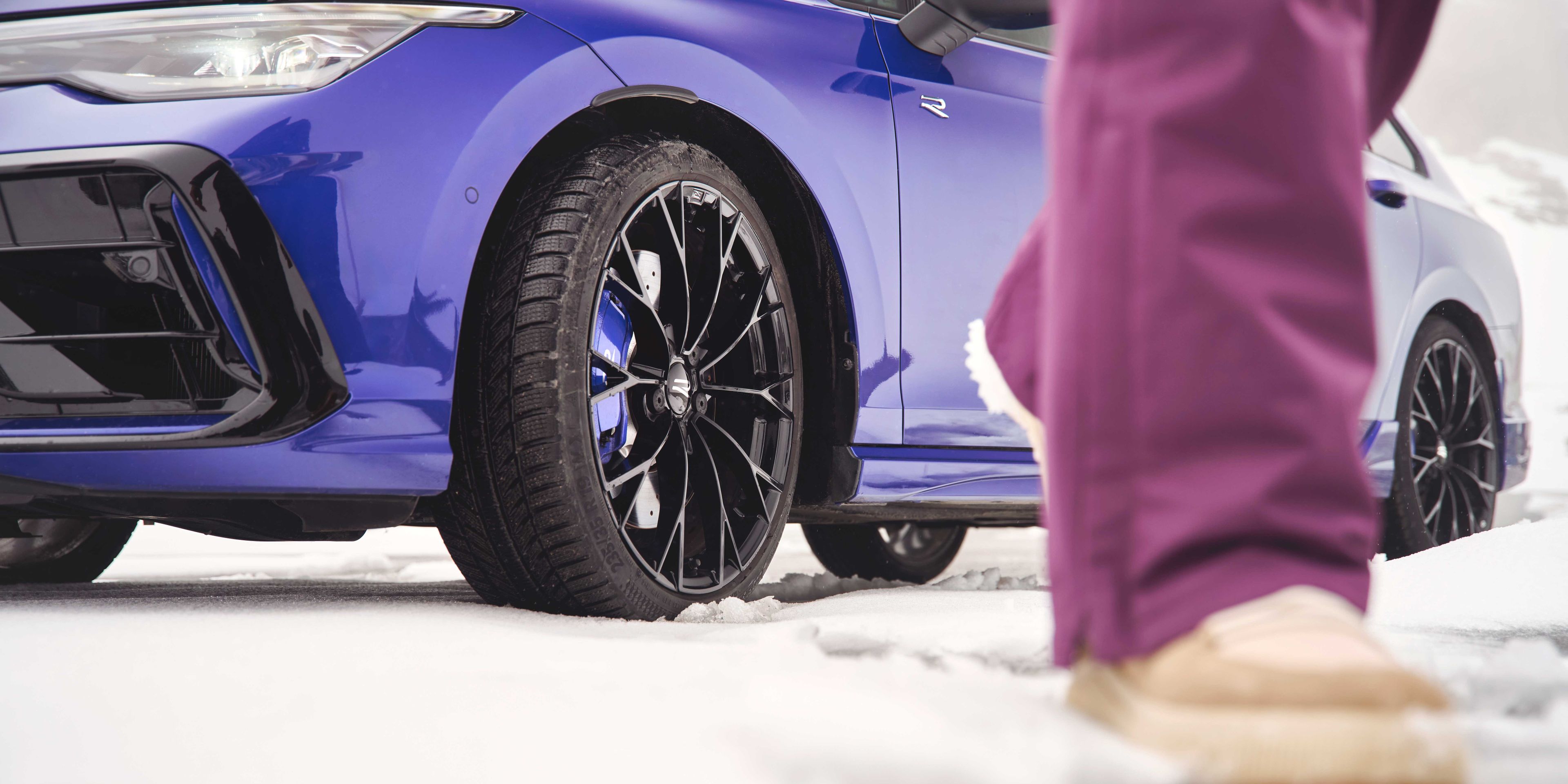 Fokusansicht der Winterkompletträder bei einem blauen Volkswagen Tayron. Im Vordergrund sind die Beine einer Person zu sehen.