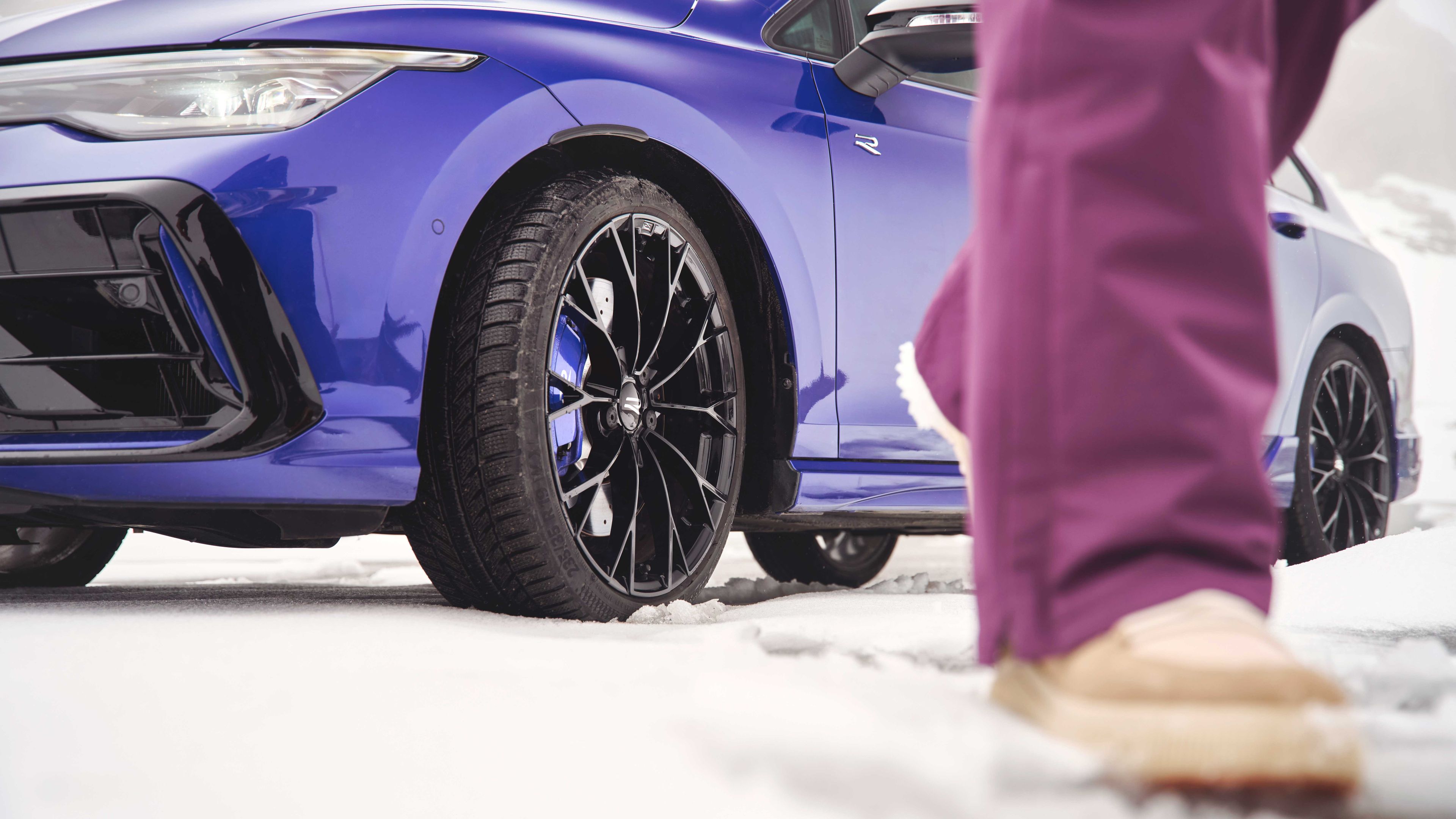 Fokusansicht der Winterkompletträder bei einem blauen Volkswagen Tayron. Im Vordergrund sind die Beine einer Person zu sehen.