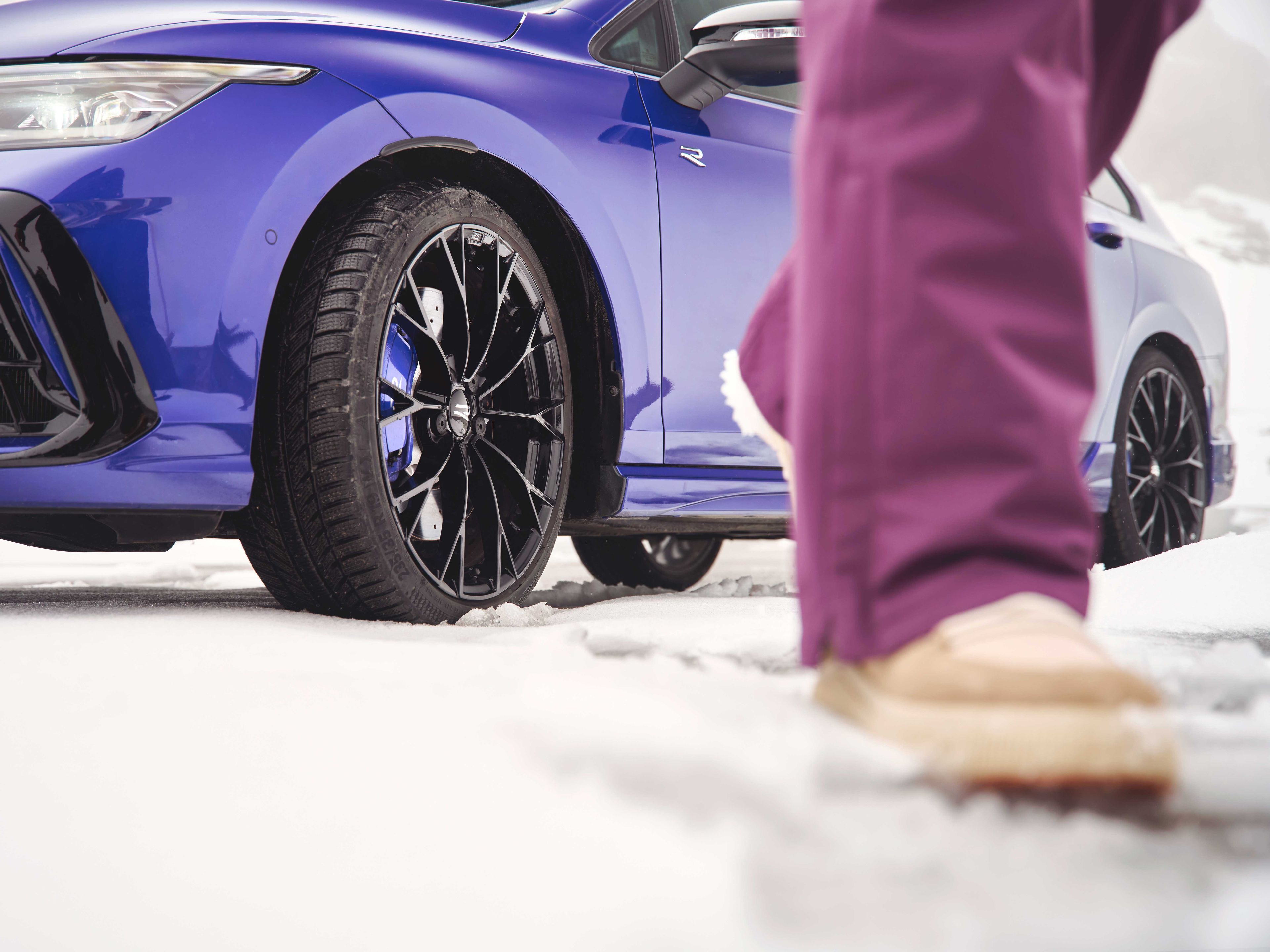 Fokusansicht der Winterkompletträder bei einem blauen Volkswagen Tayron. Im Vordergrund sind die Beine einer Person zu sehen.