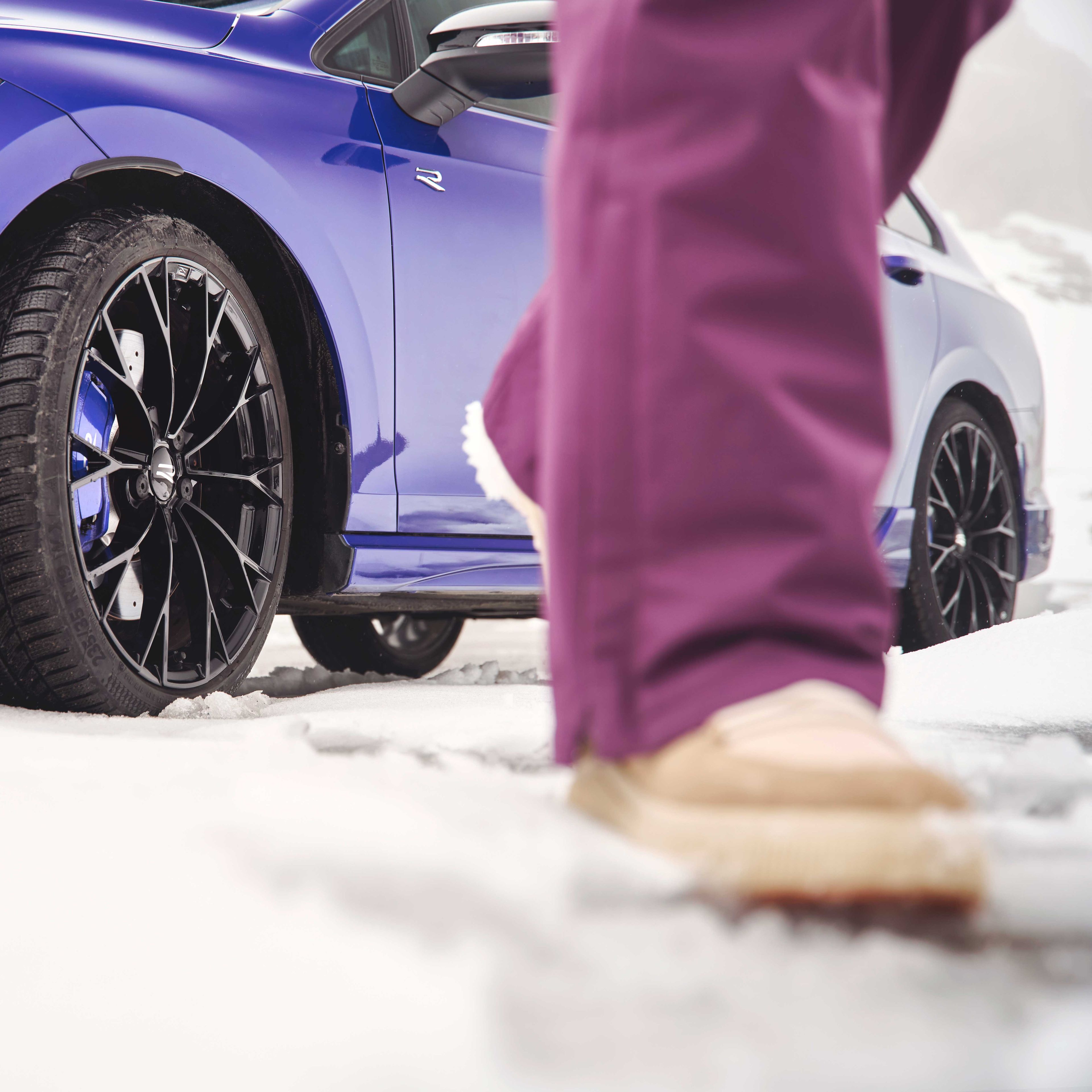 Fokusansicht der Winterkompletträder bei einem blauen Volkswagen Tayron. Im Vordergrund sind die Beine einer Person zu sehen.