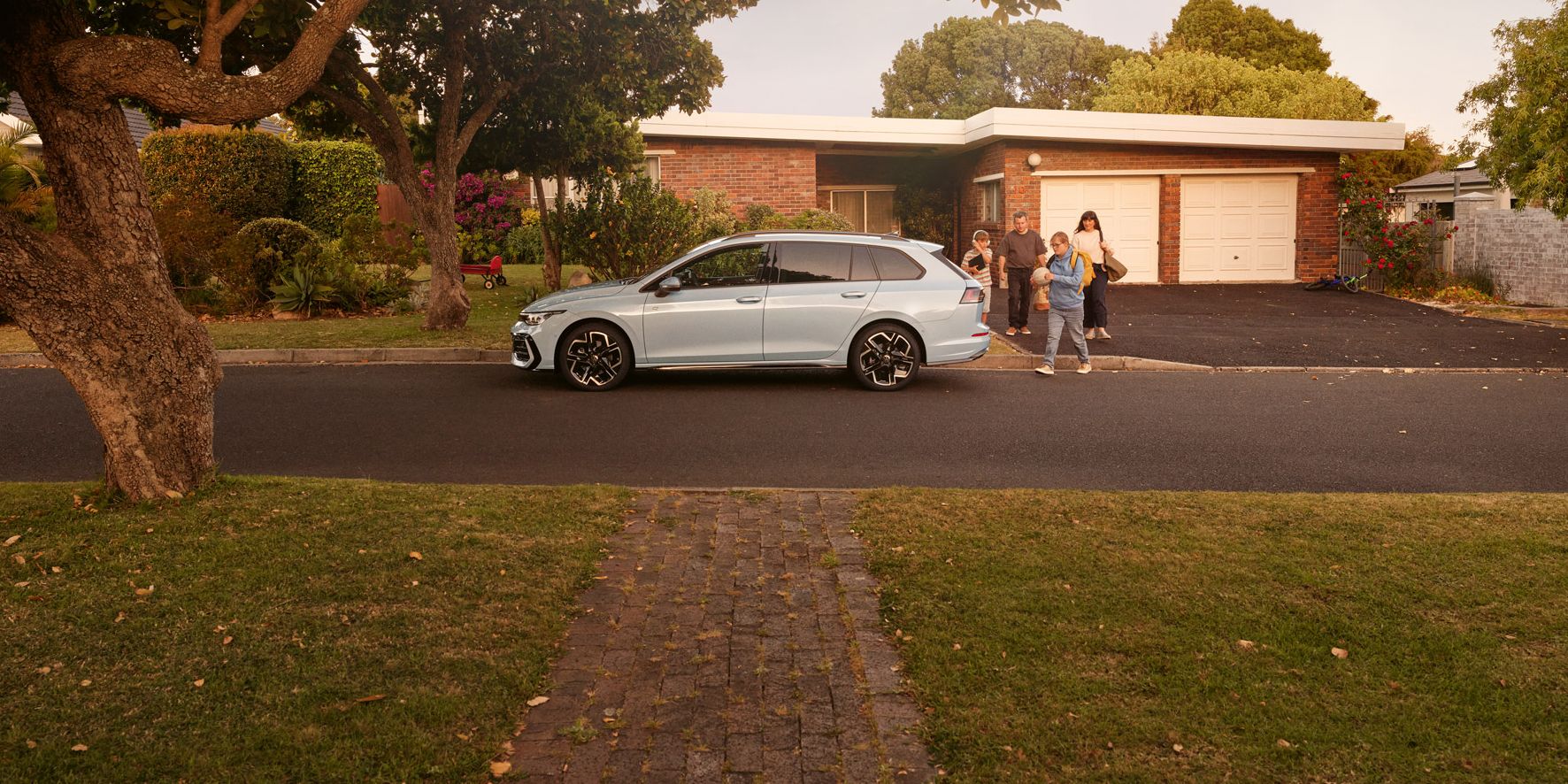 Ein weißer VW Golf Variant parkt vor einem Bungalow in einer Wohnstraße mit Bäumen. 