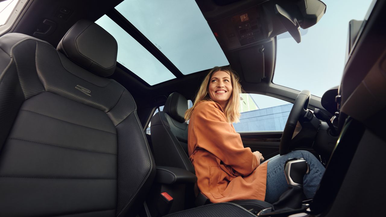 Frau sitzt in T-Roc R-Line mit Panoramadach und grinst