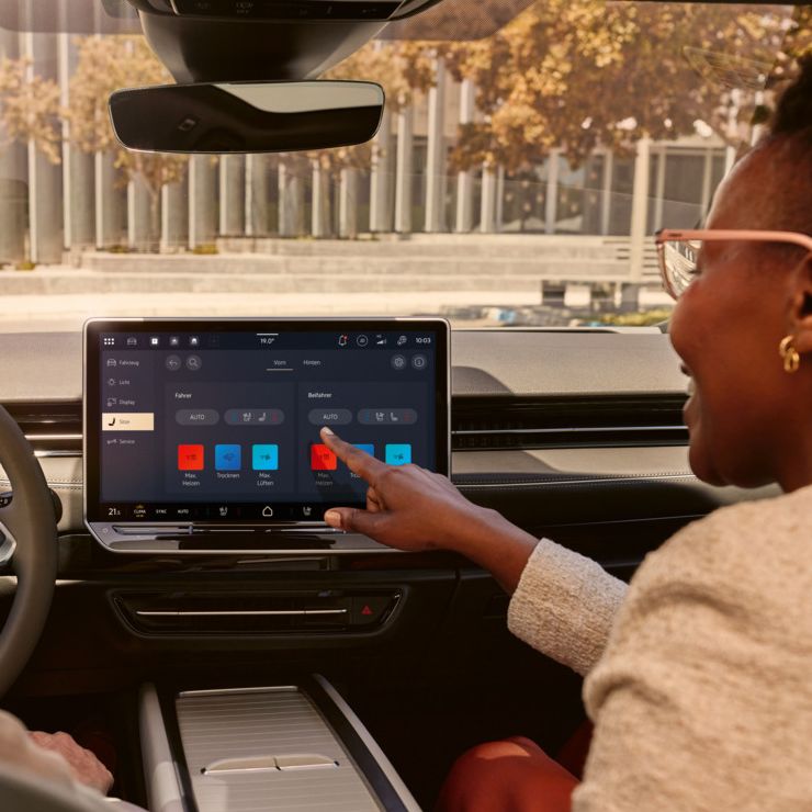 Zwei Frauen, die lachen, sitzen auf den Vordersitzen im VW ID.7 und bedienen das Infotainment-System.