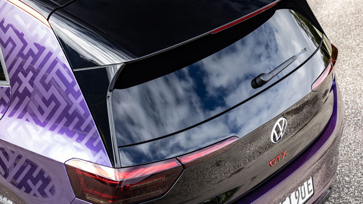 Ansicht auf das Heck eines dunkelvioletten Volkswagen ID.3 GTX. Das Auto ist auf einer Straße geparkt und zeigt reflektierende Elemente auf dem Lack. Am Heck befindet sich der Schriftzug "GTX".