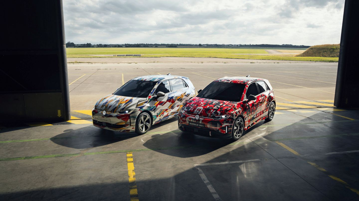 Frontale Sicht auf den ID. Polo und ID. Polo GTI. Beide Fahrzeuge sind bunt foliert und stehen in einem Hangar.