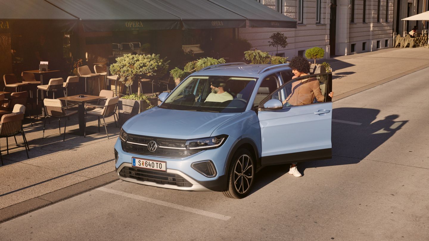 Eine Frau steigt in einen blauen VW T-Cross, der vor einem Straßencafé parkt.