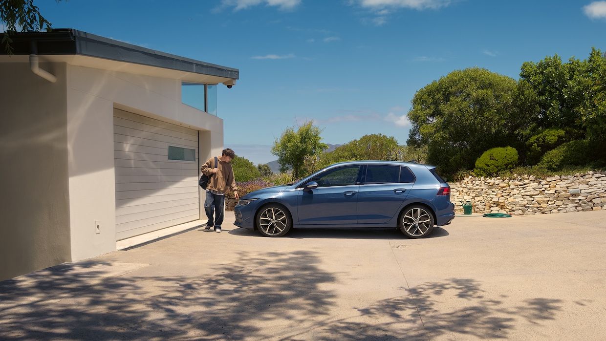 Ein junger Mann geht an einem blauen VW Golf vorbei