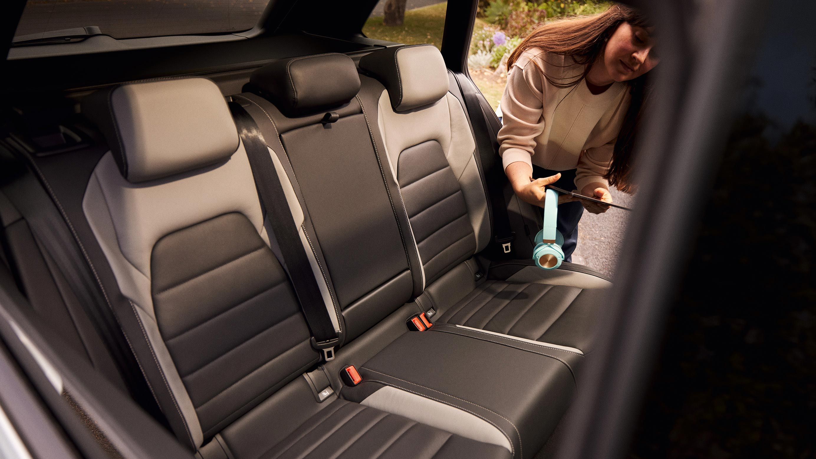 Eine Frau mit Kopfhörer und Tablet in der Hand steigt durch die hintere Fahrzeug-Tür in den VW Golf Variant ein.