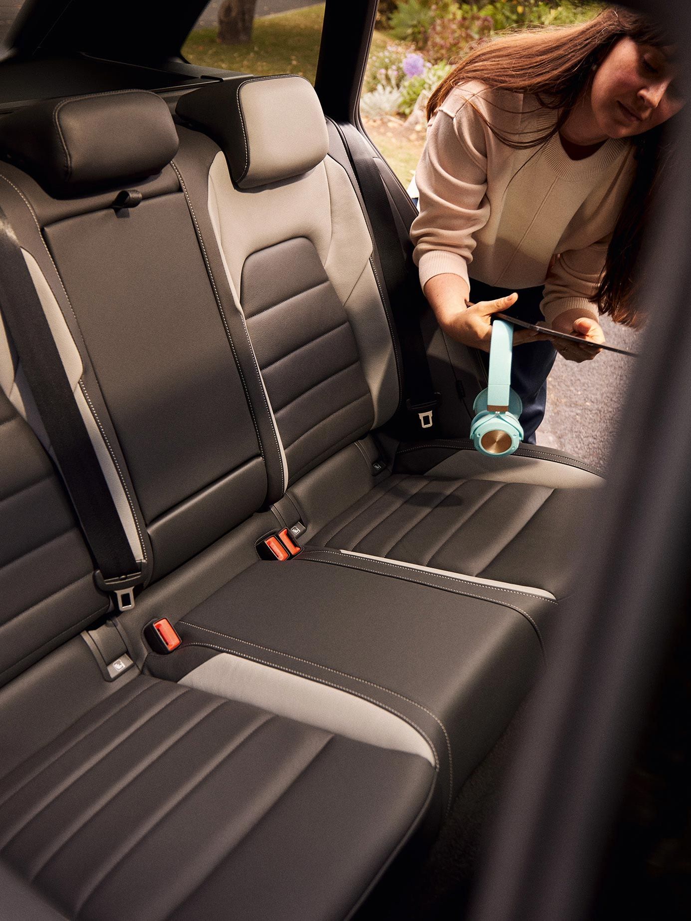 Eine Frau mit Kopfhörer und Tablet in der Hand steigt durch die hintere Fahrzeug-Tür in den VW Golf Variant ein.
