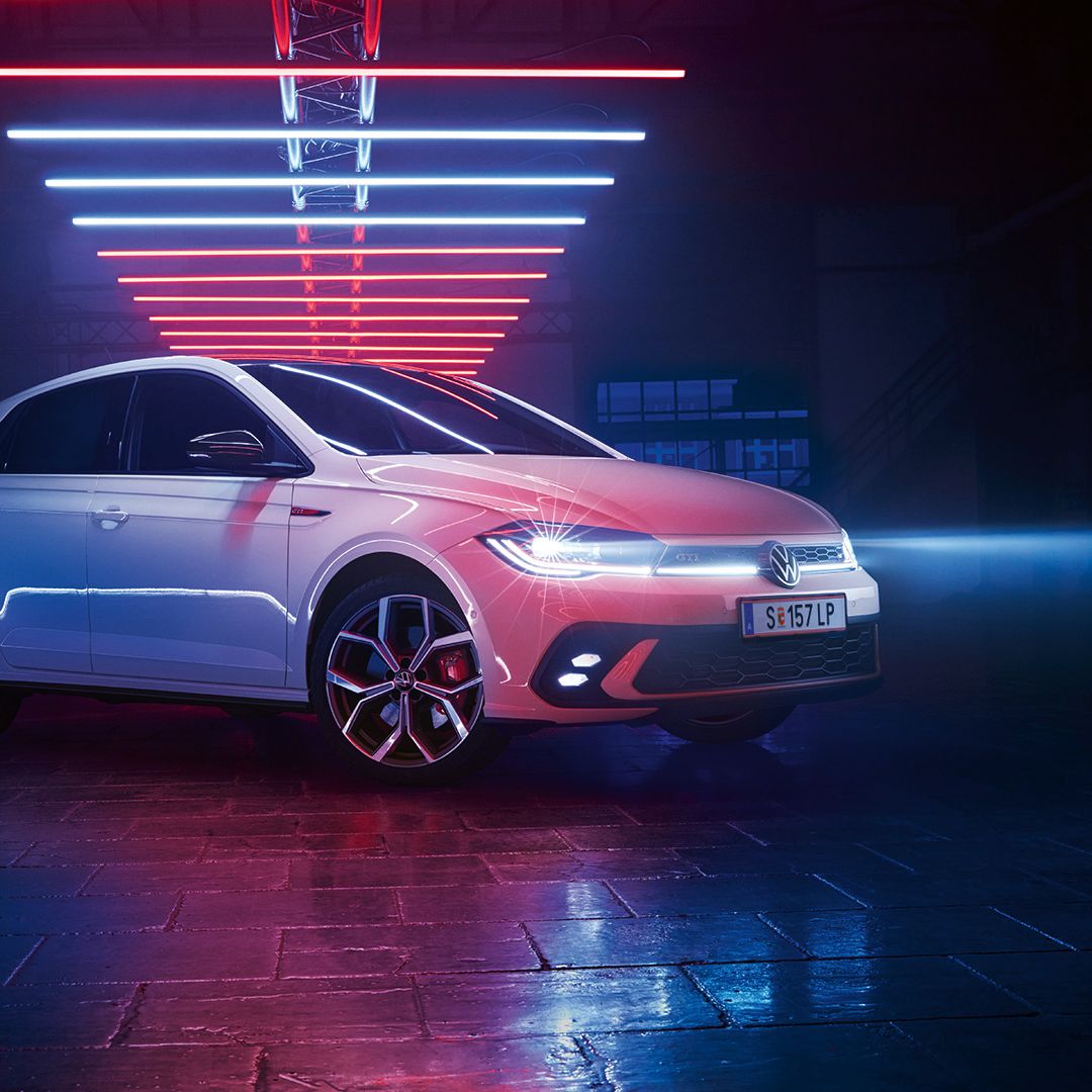 Ein weißer VW Polo GTI mit aktiven Scheinwerfern in einer dunklen Lagerhalle.