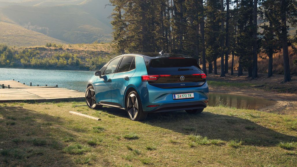 Ein blauer ID.3 steht am Ufer eines Sees, umgeben von hohen Bäumen.