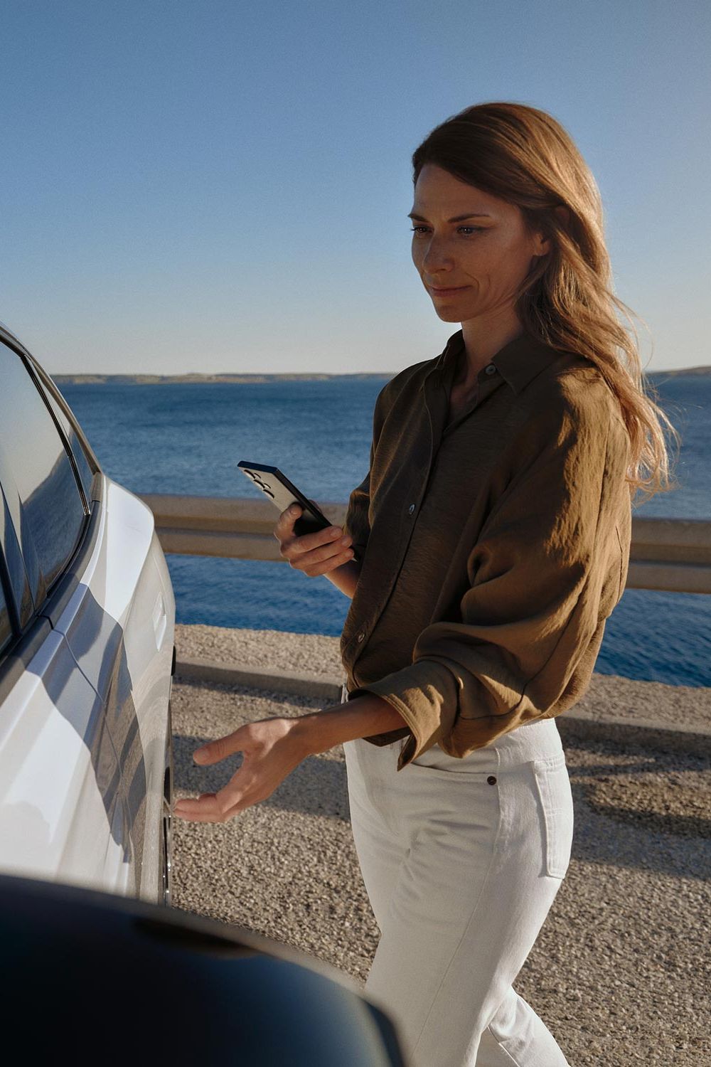 Eine Frau geht zu einem weißen VW ID.7 und öffnet die Tür. 